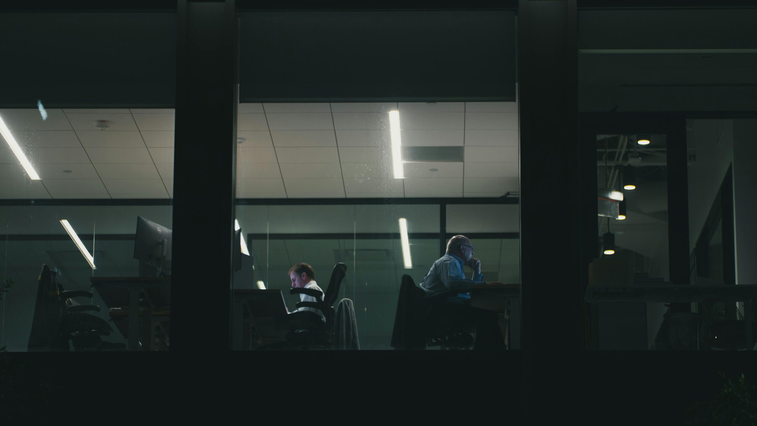 Two people working late in a modern Houston office building, visible through a window.